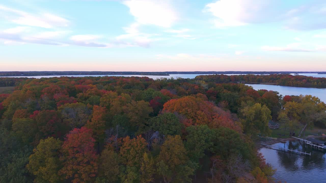 Flying over Lake Minnetonka, the shoreline bursts with autumn hues, showcasing a striking mix of red, orange, and yellow trees along the calm water