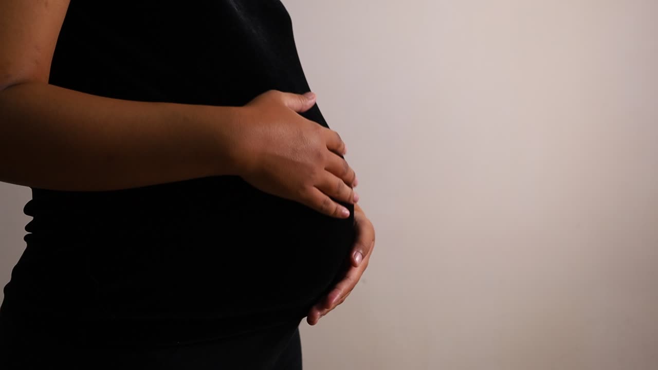 Donna incinta che si accarezza la pancia, in piedi isolata su sfondo bianco con spazio per il testo