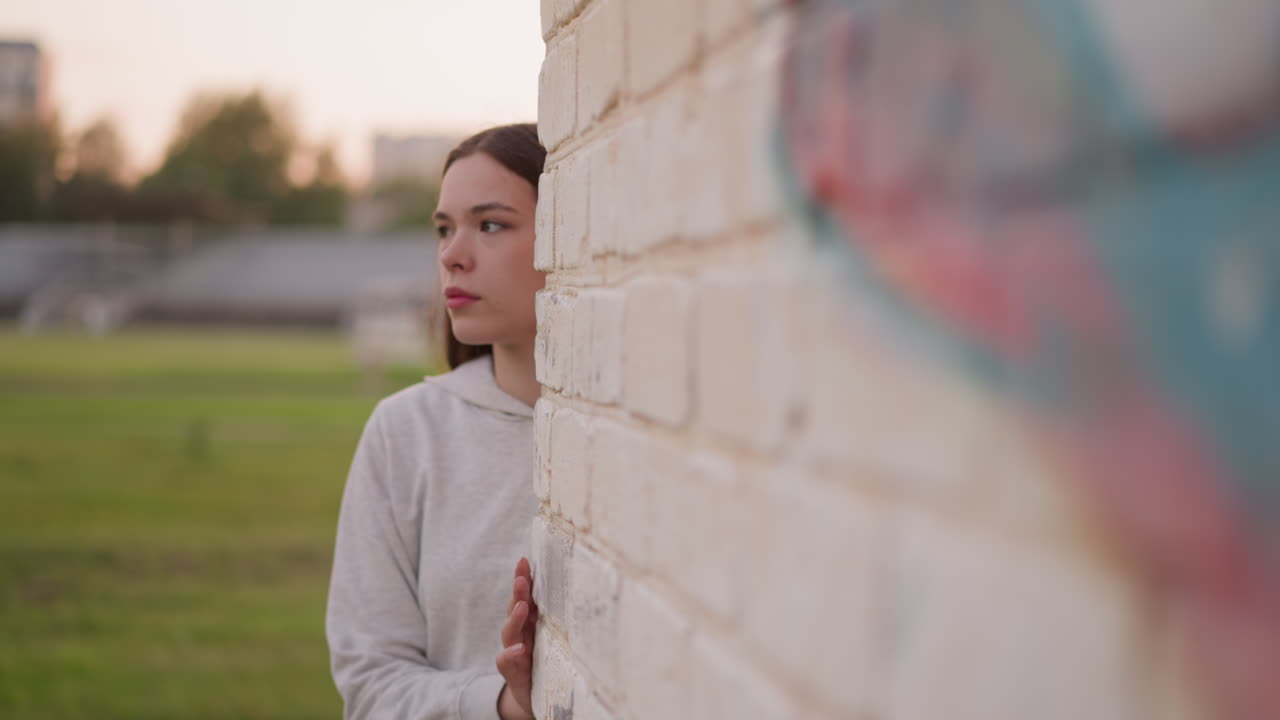 Woman comes out of graffiti wall of stadium building. Young woman afraid meeting people while in depression. Searching for secluded spot for escaping