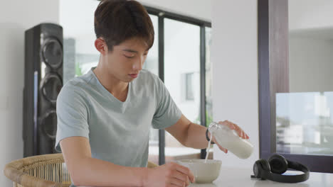 asian male teenager sitting at table alone and having breakfast