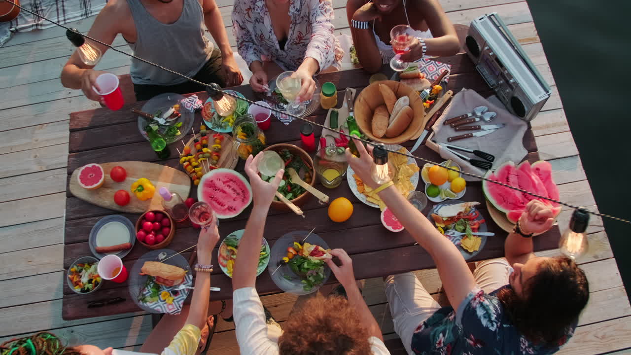 vista superior de amigos brindando en la mesa de la cena en la fiesta del lago