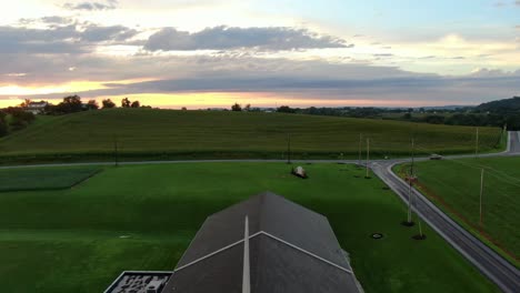 Easter-scene,-aerial-rising-into-heaven-sunset-sunrise,-Christian-cross-representing-Jesus'-death-and-resurrection,-church-and-steeple-in-green-American-rural-countryside