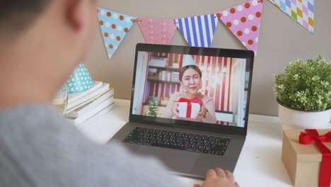 asian woman giving gift or present to friends and family via video call conference. new normal for birthday, christmas and new year party