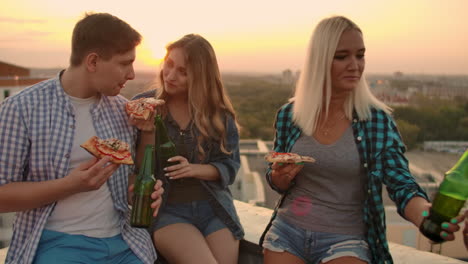 two couples in love eat pizza and drink beer on the roof. girls shyly look at their boyfriends.