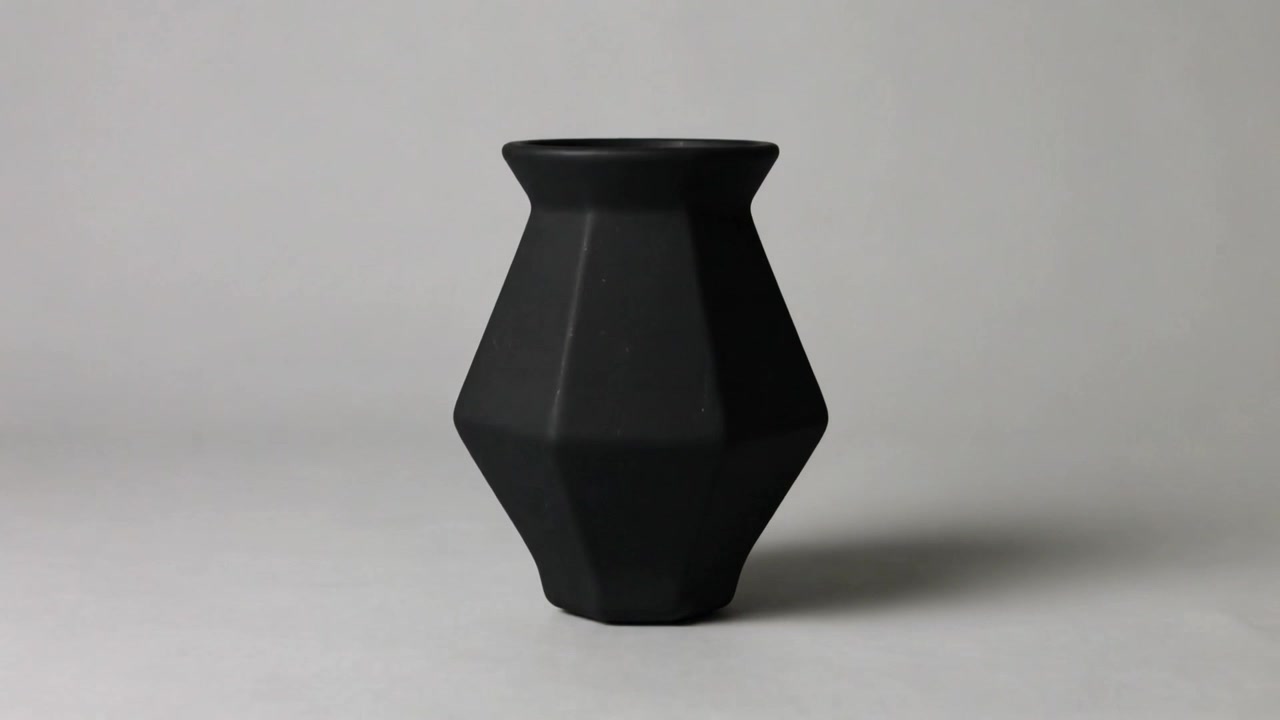 Vaso de cerâmica facetado em rotação, mudando de preto para branco após ser cortado em um pedestal de estúdio, exibindo sua forma.