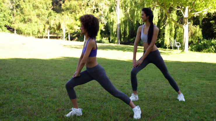 Smiling fit friends stretching legs in the park