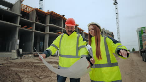 Eine-Bauingenieurin-Und-Ein-älterer-Professioneller-Vorarbeiter-Besprechen-Den-Bauplan-Auf-Der-Baustelle