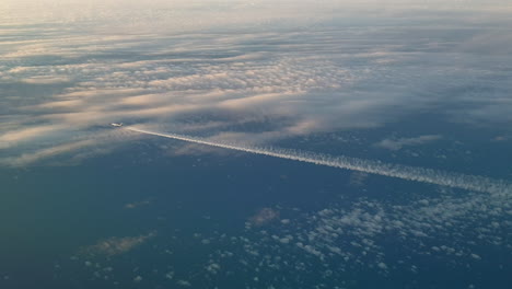 Vista-Increíble-Desde-La-Cabina-De-Un-Avión-Que-Vuela-Alto-Por-Encima-De-Las-Nubes-Dejando-Un-Largo-Rastro-De-Aire-De-Vapor-De-Condensación-Blanco-En-El-Cielo-Azul