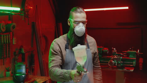 caucasian man in goggles, respiratory mask and apron working with pulverizator in workshop