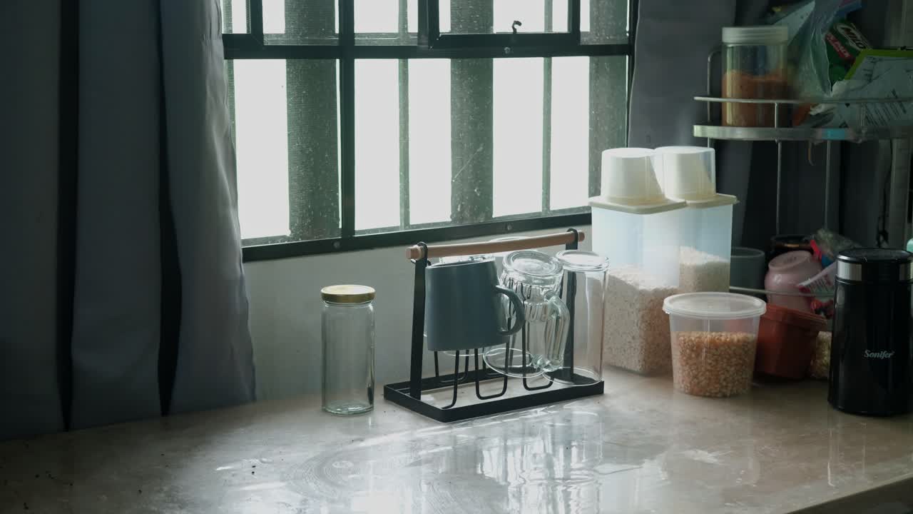 Scenic view of a person clearing mugs and glasses from sunlit kitchen table for cleaning. -medium static shot