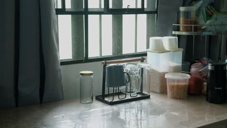 scenic view of a person clearing mugs and glasses from sunlit kitchen table for cleaning. -medium static shot