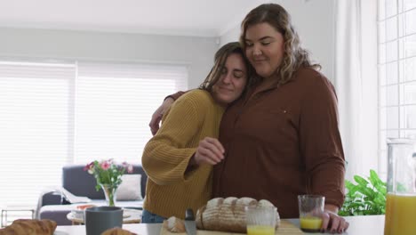 pareja de lesbianas caucásicas abrazándose y sonriendo en la cocina