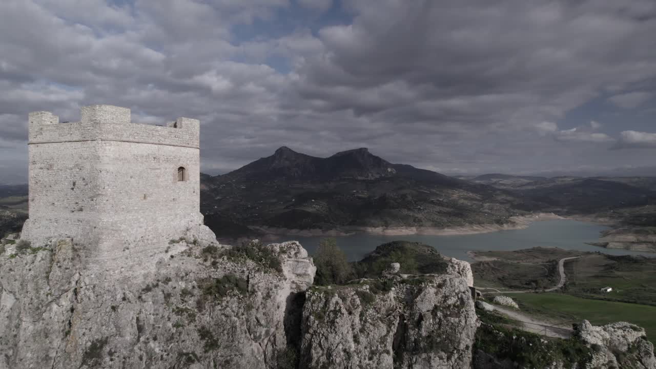 4K drone shot of Zahara de la Sierra, Spain, filmed with a DJI at 30fps. A cinematic backward flight revealing the medieval castle, the stunning reservoir, and the village below.