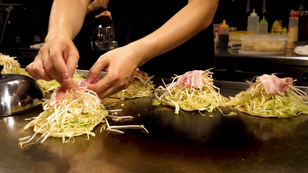Uno chef giapponese cucina una tradizionale frittella salata Okonomiyaki su una piastra teppanyaki a Kyoto, Giappone