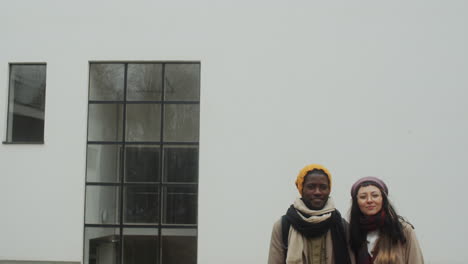 happy multiethnic couple posing against white building