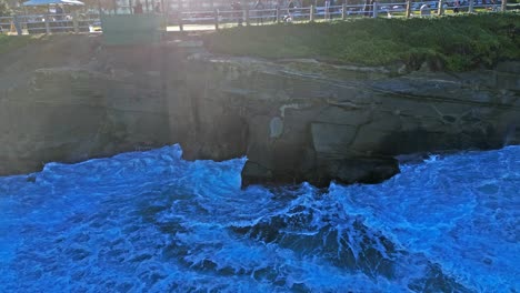 Drone-shot-of-wave-crashing-on-cliff-with-big-splash-towards-camera-during-high-tide-in-La-Jolla-California