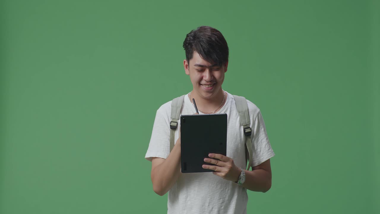 아시아 남성 학생이 태블릿에 글을 쓰고 녹색 스크린 스튜디오에서 고 있습니다.