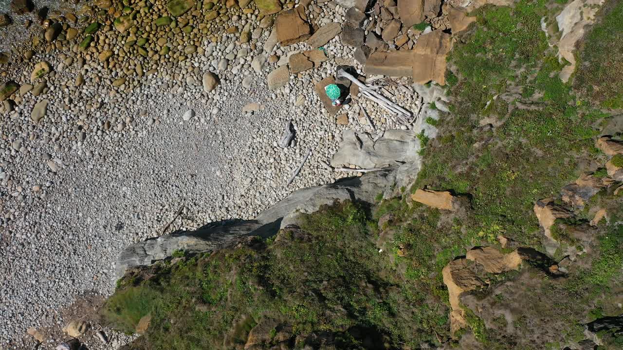fotografía superior en un acantilado a lo largo de la cual una escalera corre que baja a la playa de piedra donde se pueden ver algunos paraguas y las olas del mar chocando tranquilamente contra las rocas en cantabria españa