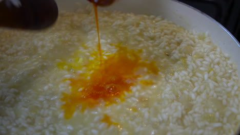 italian chef pouring a yellow saffron mixture with pistils into risotto milanese
