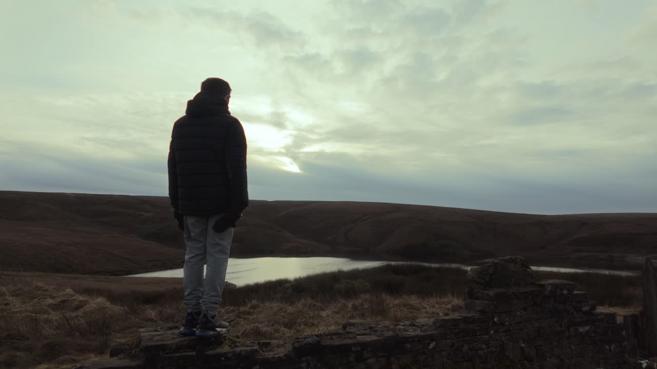 niño de pie y mirando hacia el paisaje de invierno, con páramos, pantanos, un lago y un cielo de inviernos tormentosos