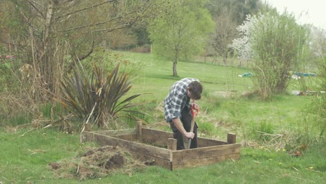 wide shot of young man removing top soil with shovel building raised garden bed