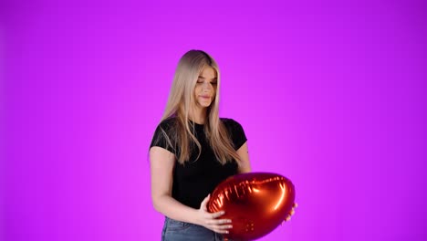 una linda mujer rubia abraza un corazón de globo rojo y lo lanza en el aire, toma de estudio