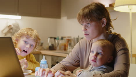 mother of two kids working on laptop at home