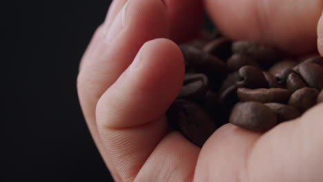 mano caucásica sosteniendo un montón de granos de café tostados e inspeccionando los granos con el pulgar
