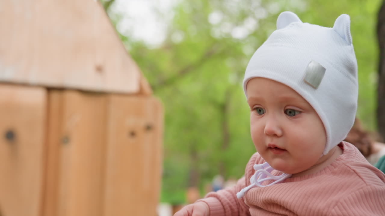 Curious Infant Watching, Inquisitive Baby Wearing Hat Attentively Observes Nearby Scenery, White Infant With Bright Expressive Eyes Eagerly Explores Outdoor Park Surroundings In Detail