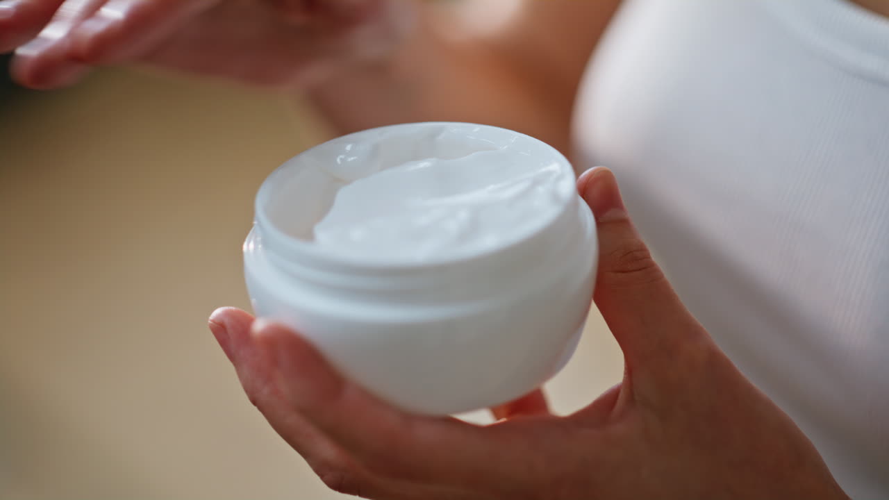 Woman hand taking moisturizing cosmetic cream from jar at home skincare closeup