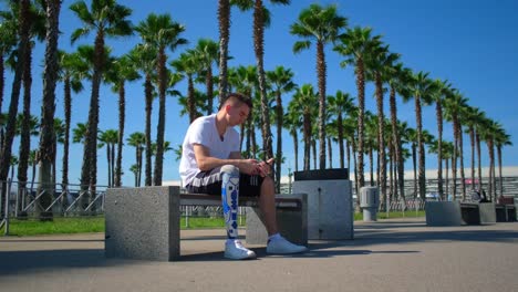 hombre con pierna protésica usando un teléfono inteligente en un parque