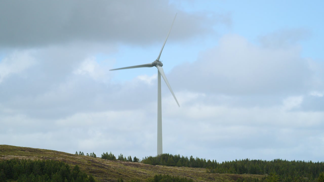 Static shot of an active wind turbine turning on a moorland hillside.
