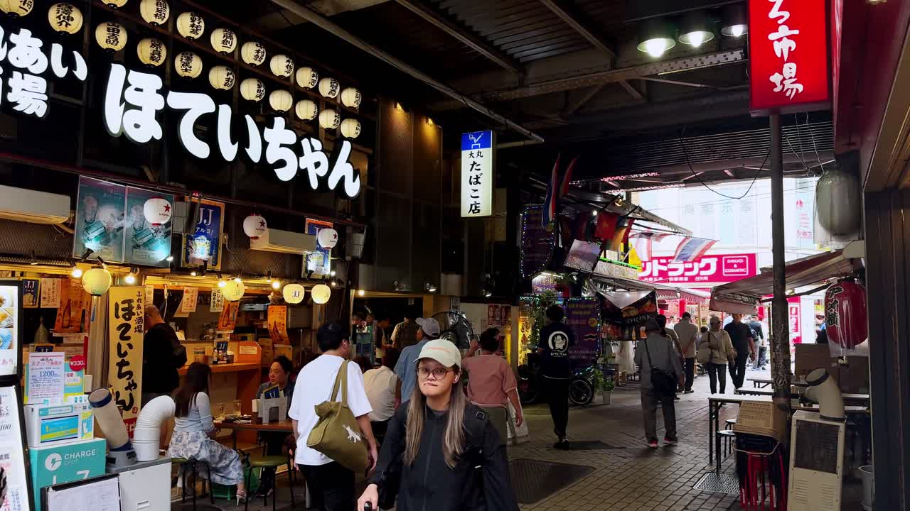 Bustling Japanese market street with lanterns, restaurants, and people walking by under signs