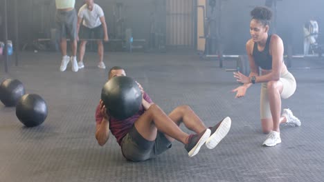 Entrenadora-Diversa-Motivando-A-Un-Hombre-Decidido-A-Hacer-Ejercicio-Con-Balón-Medicinal-En-El-Gimnasio,-En-Cámara-Lenta