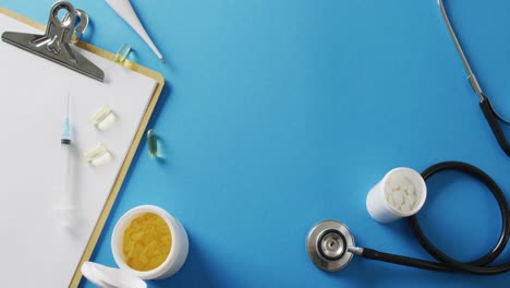 video of stethoscope, clipboard, syringe, capsules and pills on blue background with copy space