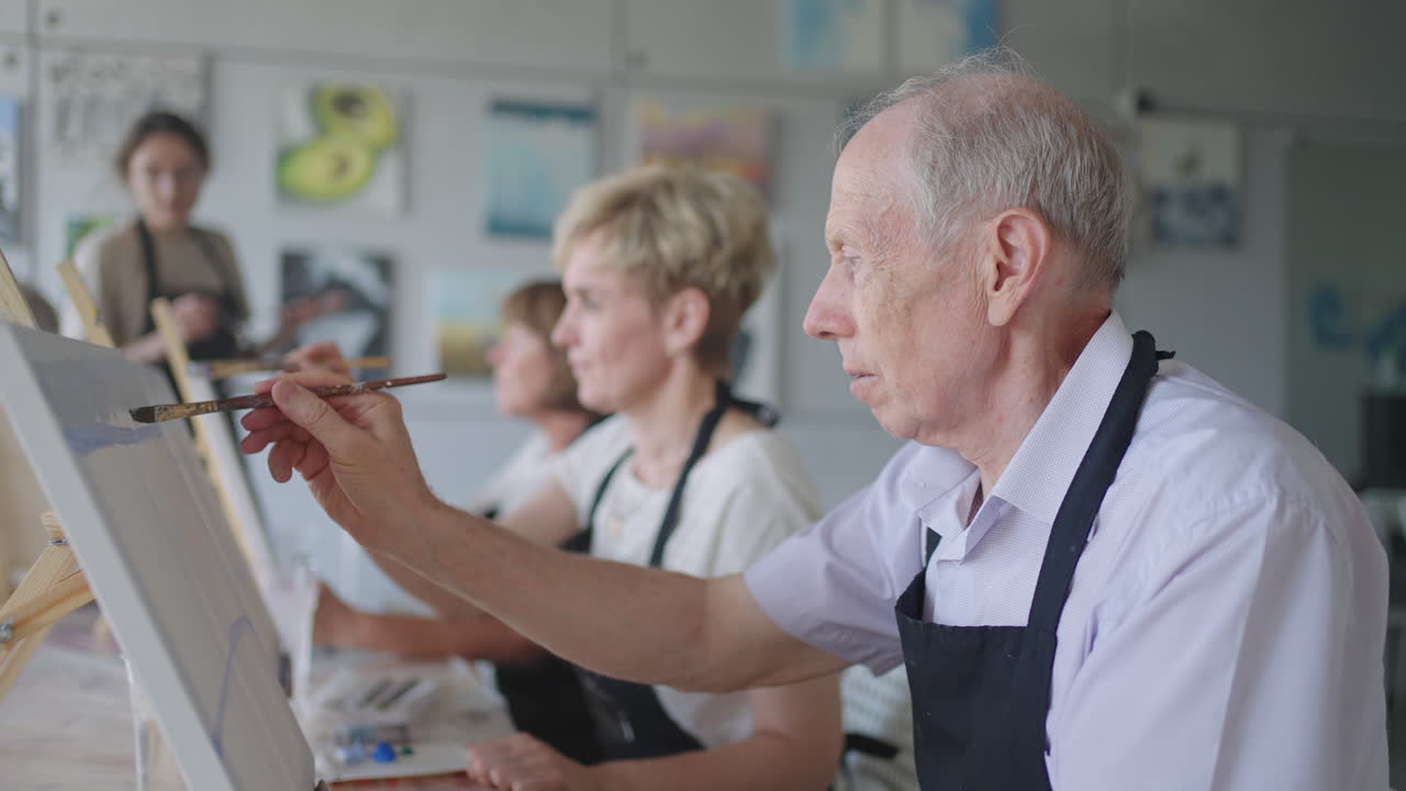 vista de ángulo alto de amigos mayores alegres pintando en lienzo. mujer mayor sonriendo mientras dibuja con el grupo. mayores asistiendo a clase de pintura juntos. hombres mayores divirtiéndose pintando en clase de arte