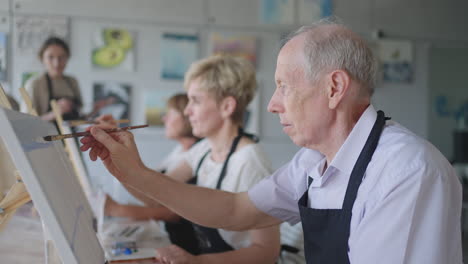 high angle view of cheerful senior friends painting on canvas. senior woman smiling while drawing with the group. seniors attending painting class together. senior men having fun painting in art class