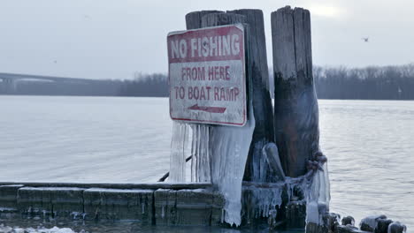 Close-up-detail-of-no-fishing-prohibition-sign-with-ice,-birds-in-background,-Static-shot