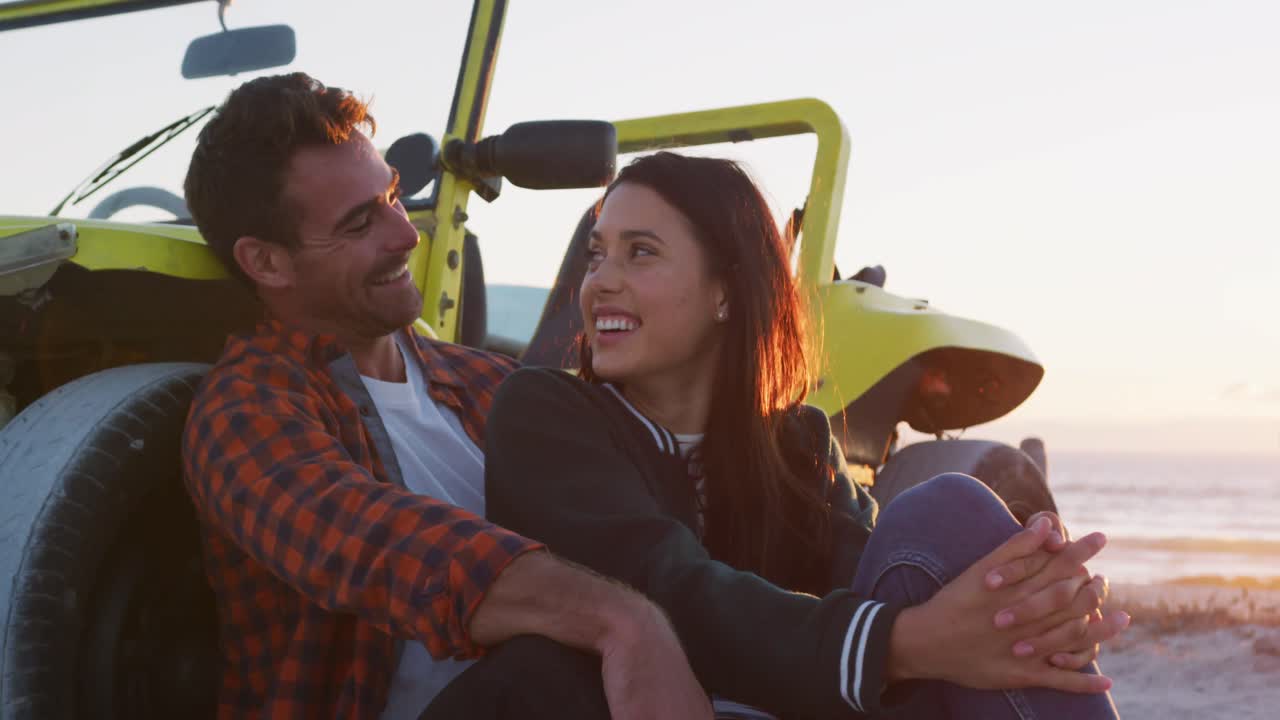 feliz pareja caucásica sentada al lado de la playa en un buggy junto al mar hablando abrazándose