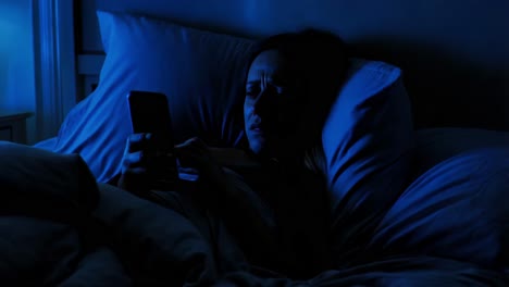 woman using phone in bed at night