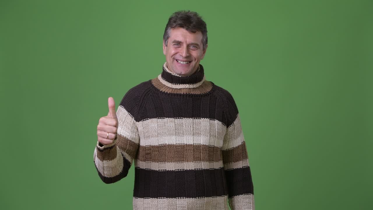 hombre guapo maduro con suéter de cuello alto contra un fondo verde