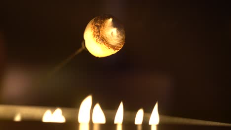 Appetizing white marshmallow warming up over gas fire pit at night, detail shot