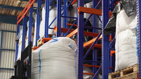 a mechanized forklift is lifting a heavy white bag to a top shelf in a fully-loaded warehouse