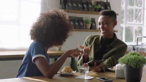 happy african american woman using tablet computer showing friend laughing together enjoying funny entertainment on mobile device screen in coffee shop