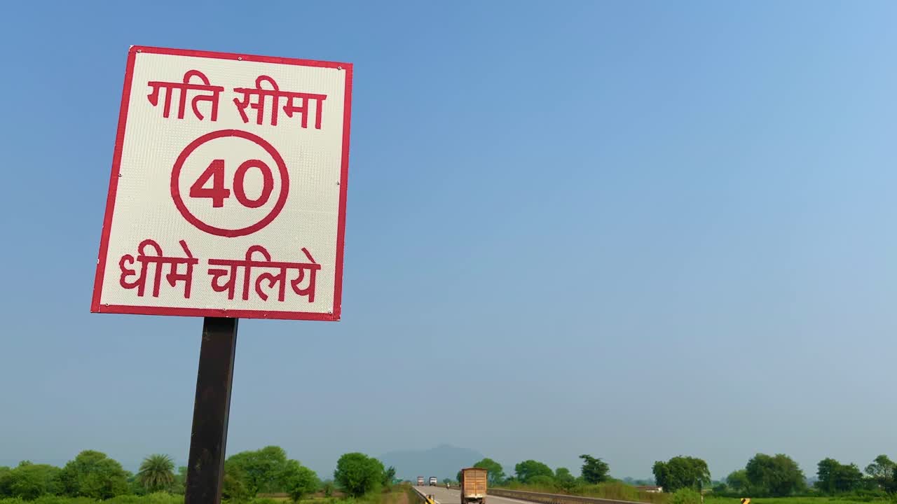 A static shot showing an Indian speed limit signboard reading “Speed Limit 40 – Drive Slowly” in Hindi, with vehicles moving in the distance on a rural highway under a clear blue sky