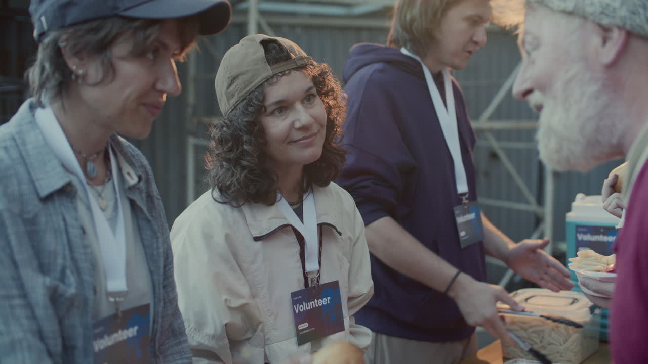 Friendly Volunteers Handing Out Hot Meals to Homeless at Street Food Station