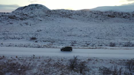 Antenne-Eines-Autos,-Das-Eine-Lange-Straße-Durch-Die-Winterliche-Isländische-Landschaft-Fährt