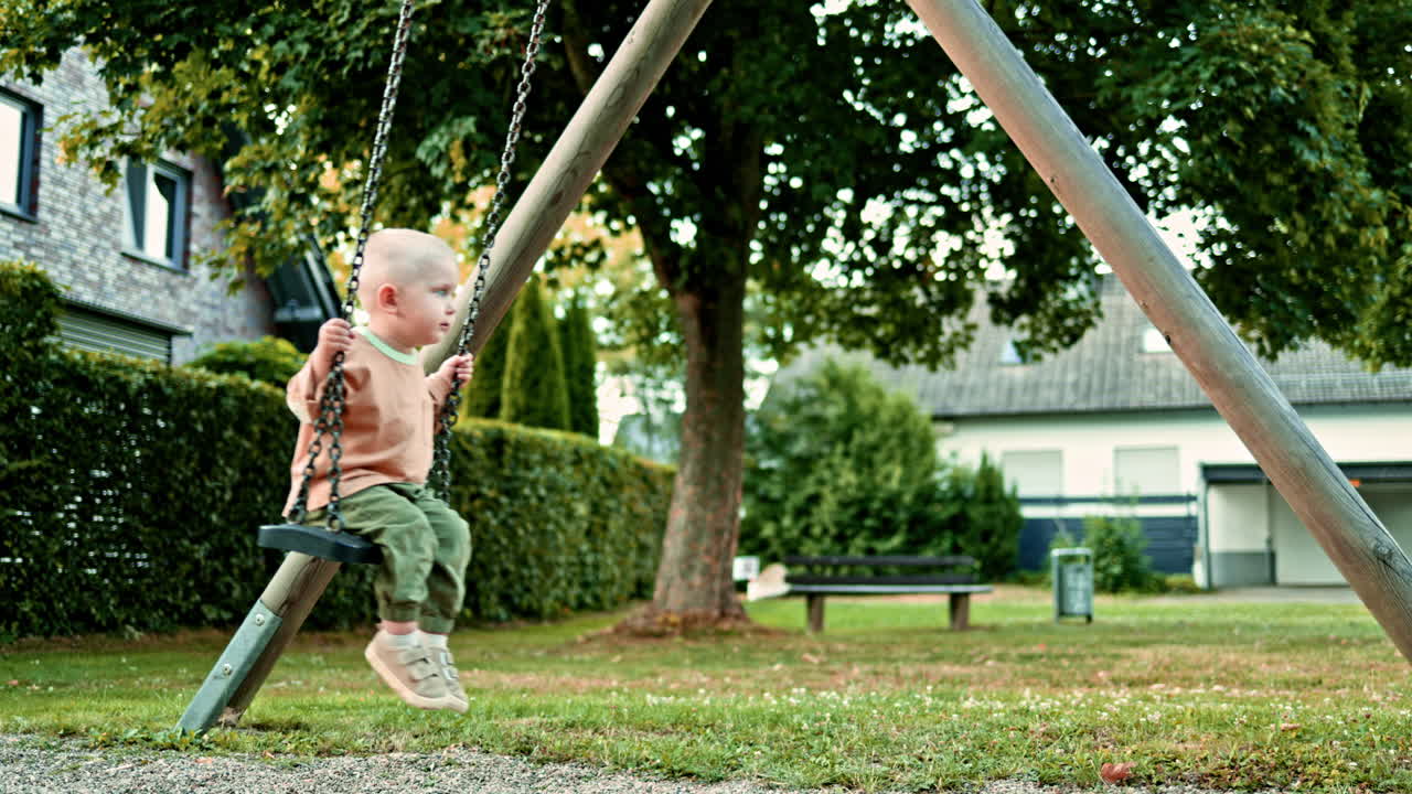 Happy boy swings on a swing on a playground in the park. The child has fun on a walk. Swing for children in a city park. Toddler boy rides on a swing in the summer. Children's entertainment