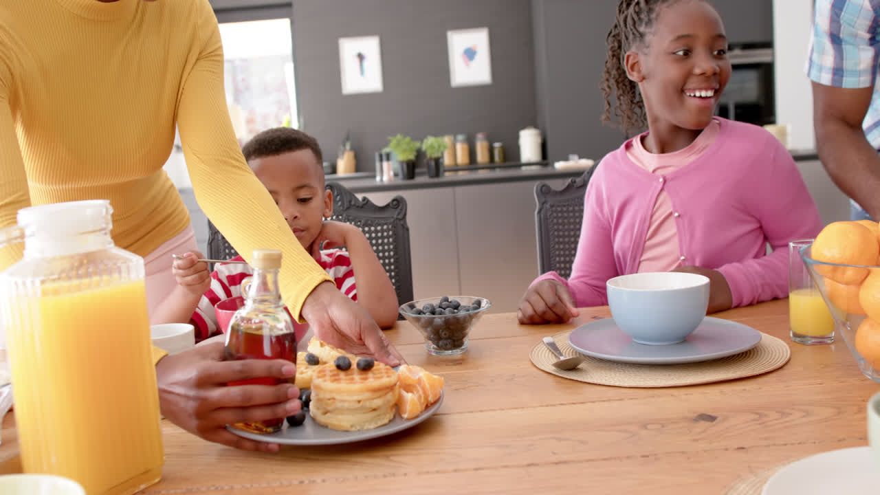 African american parents with son and daughter serving breakfast at table in kitchen, slow motion