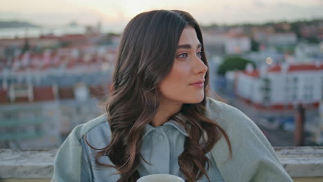 portrait serene woman looking camera at dusk cityscape. model holding coffee